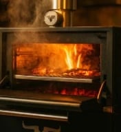 Wood-burning stove with active flames visible through glass door, clock on top, warm ambient lighting